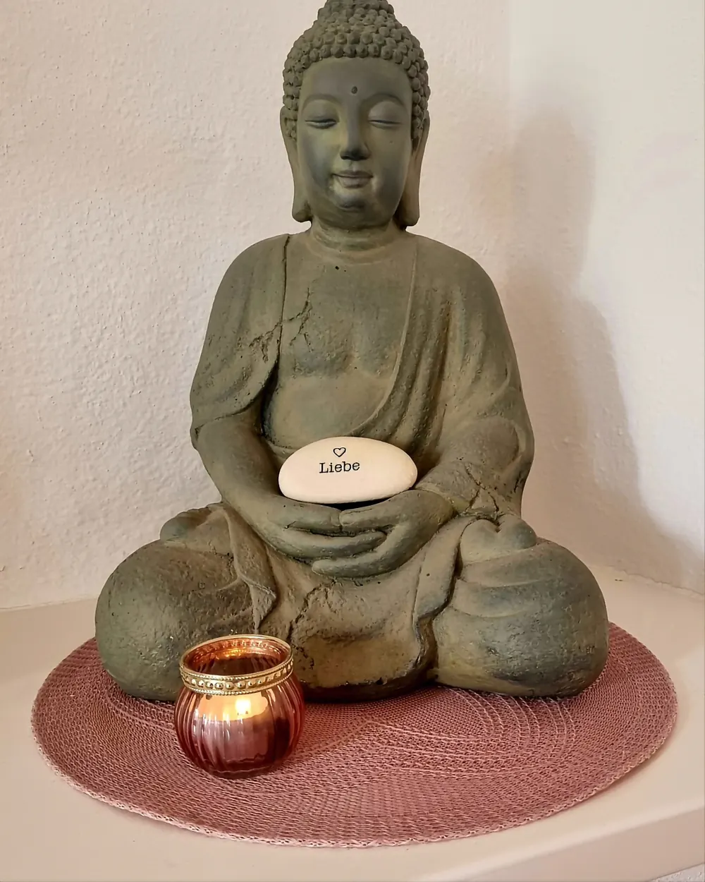 Buddha-Figur mit einem Stein mit der Aufschrift Liebe und einem Teelicht